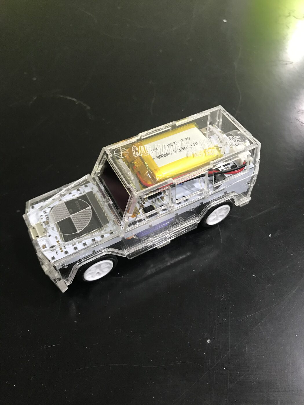 The badge unlit, showing the LiPo battery, wheels and circuit board inside the clear body