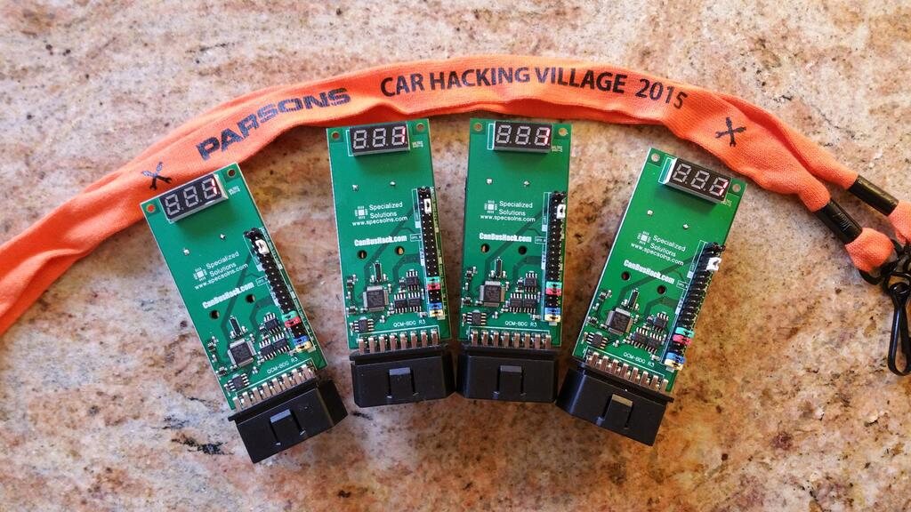 Four green Car Hacking Village badge boards with OBD-II connectors and three-digit displays, laid out with a Car Hacking Village 2015 lanyard
