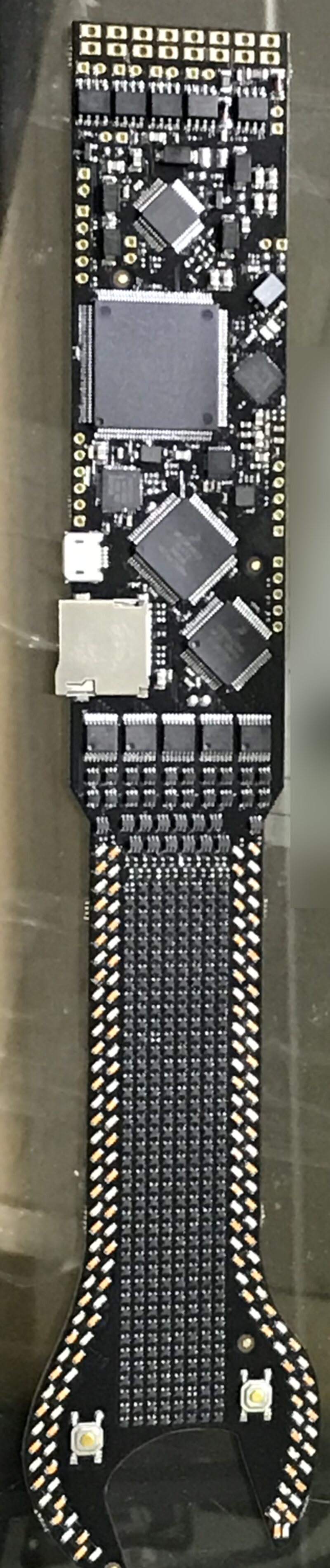 Assembled black wrench-shaped badge PCB with an LED matrix in the handle, several large ICs, a microSD slot and micro-USB
